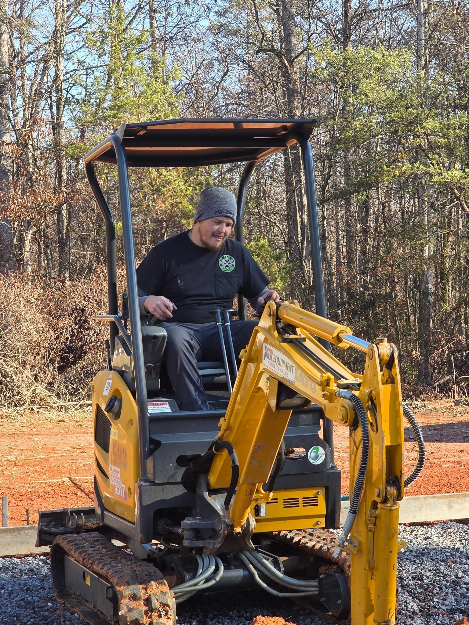 Worker in the cab of a mini excavator on a graded new construction job site.