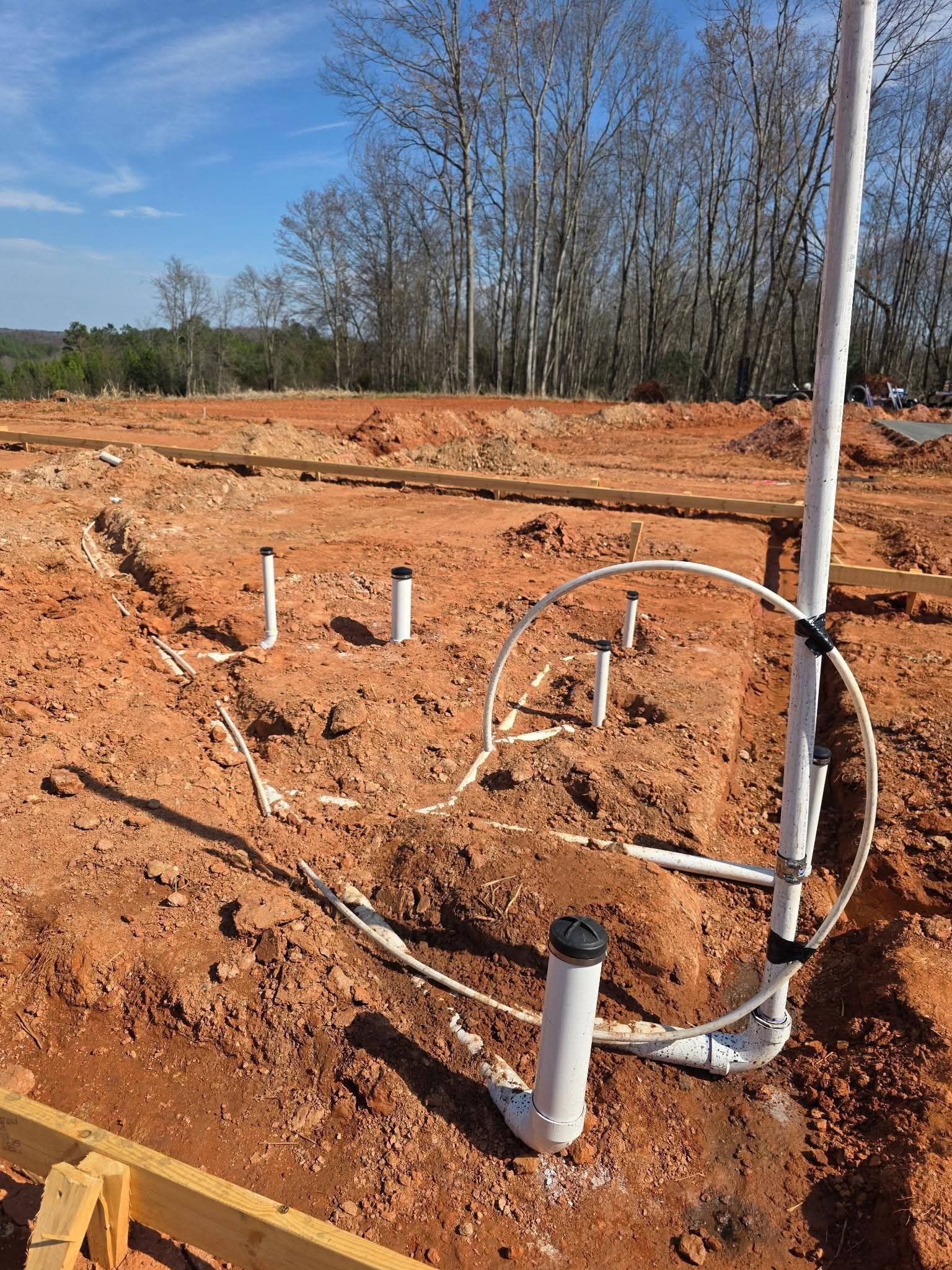 PVC pipe network with vertical stub-ups and a tall vent stack rising from the excavated foundation.