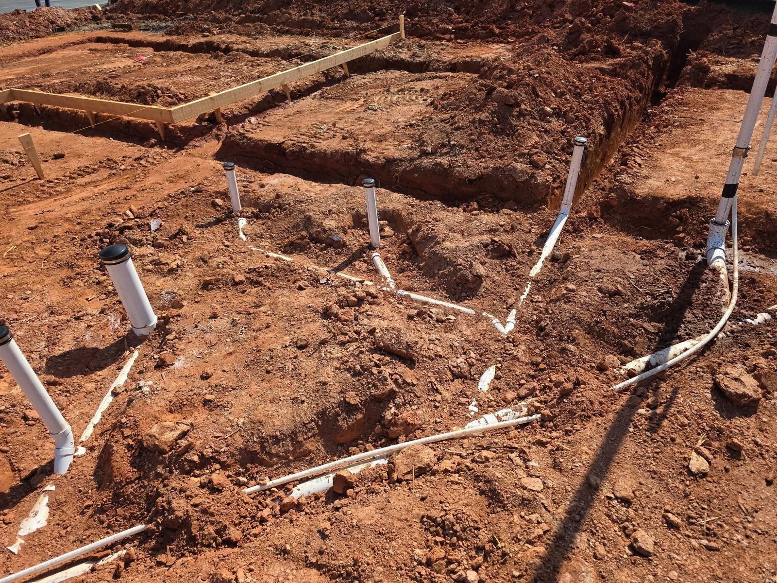 White PVC stub-up pipes and fittings arranged in a branching layout within an excavated foundation area.
