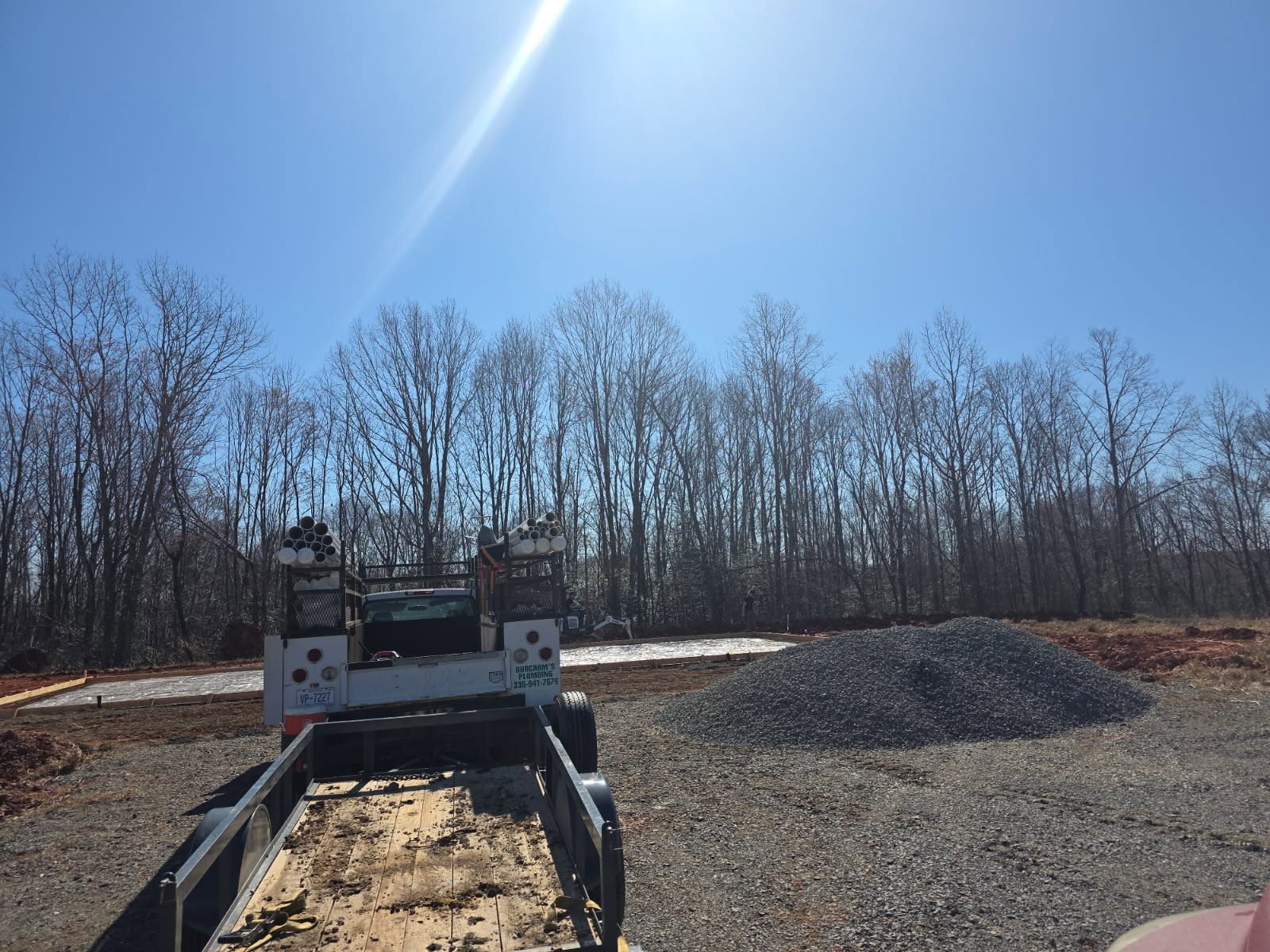Plumbing service truck loaded with pipe stock parked near a gravel pile at a residential construction site.