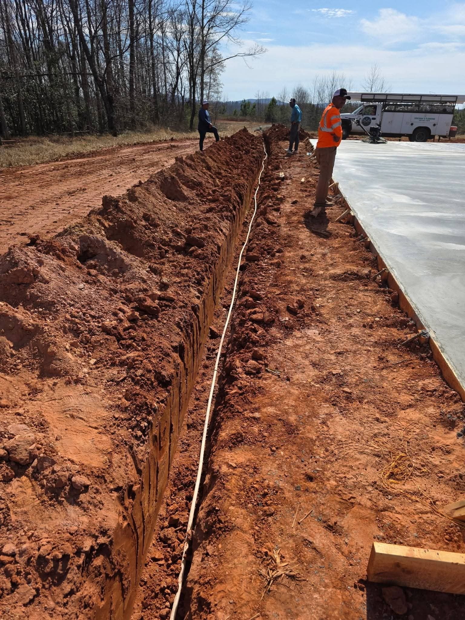 Long straight trench with pipe along the bottom running toward a poured concrete slab.