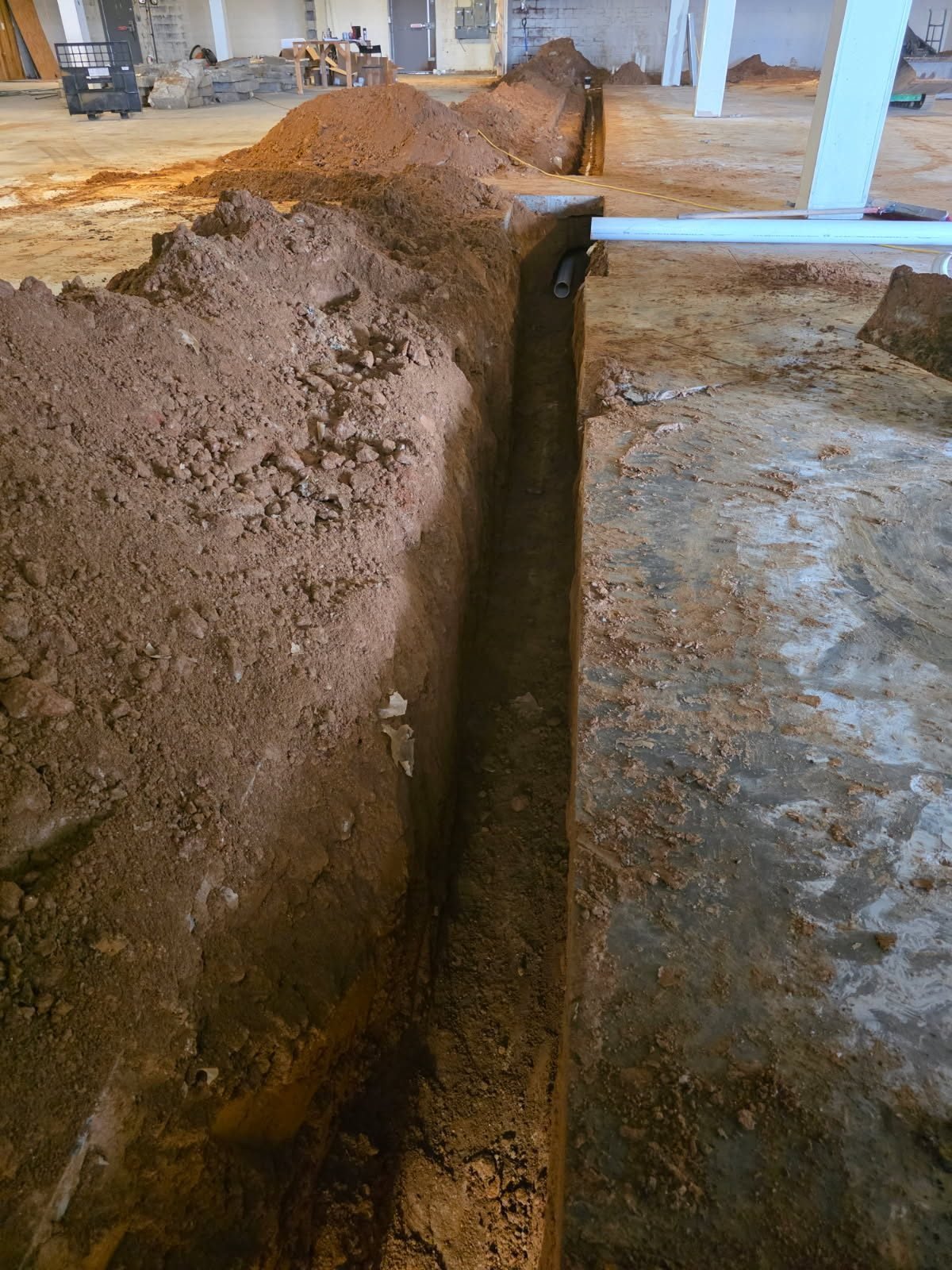 Interior trench with a pipe section laid in the bottom next to a section of clean concrete slab.