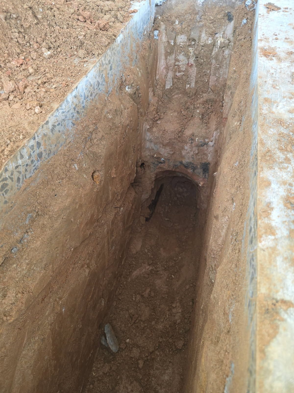Close-up view down a narrow interior trench with an opening cut into a concrete footer.