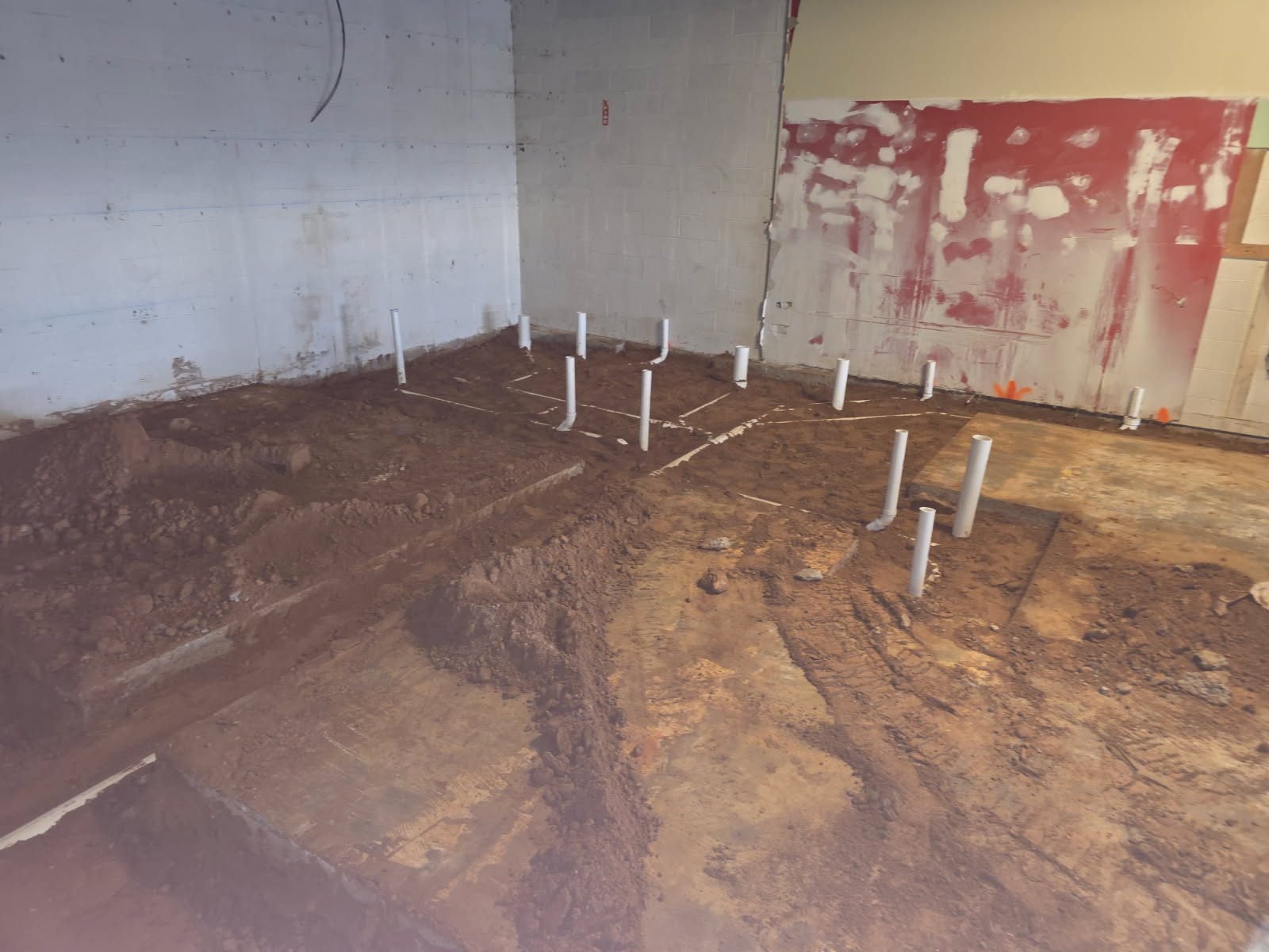 PVC stub-up pipes rising from an excavated dirt floor along interior walls, connected by marked pipe-run lines.