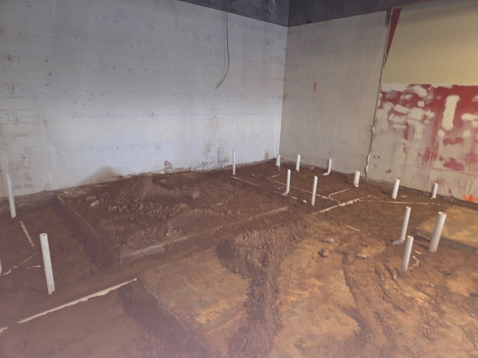 Interior view of PVC stub-up pipes spread across a dirt subgrade area, prepped for the slab pour.