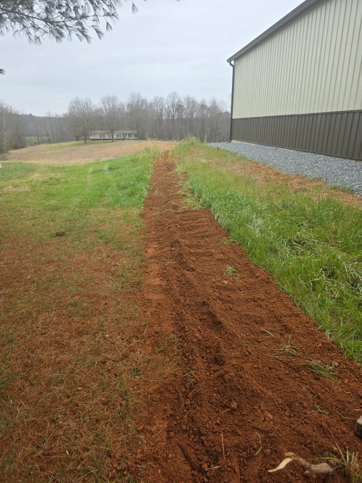 Freshly backfilled trench line running alongside a metal pole-barn building.