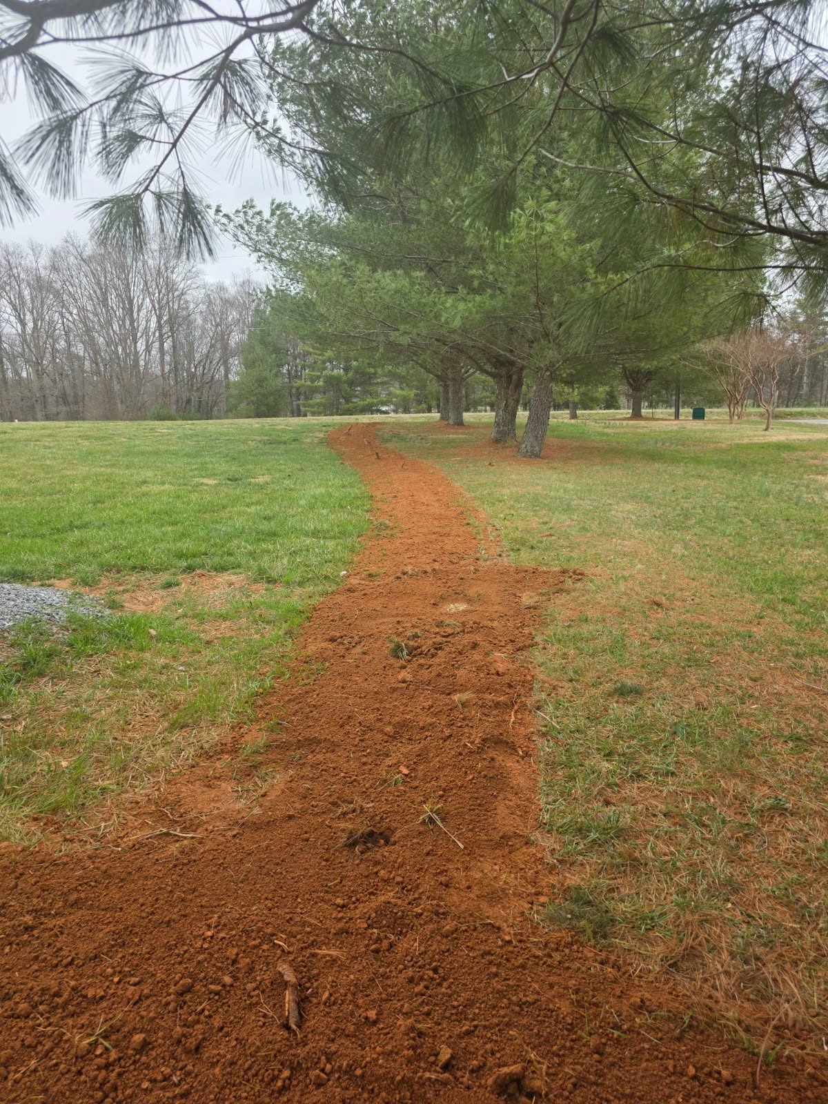 Curving trench line cut through an open grassy field with trees in the background.