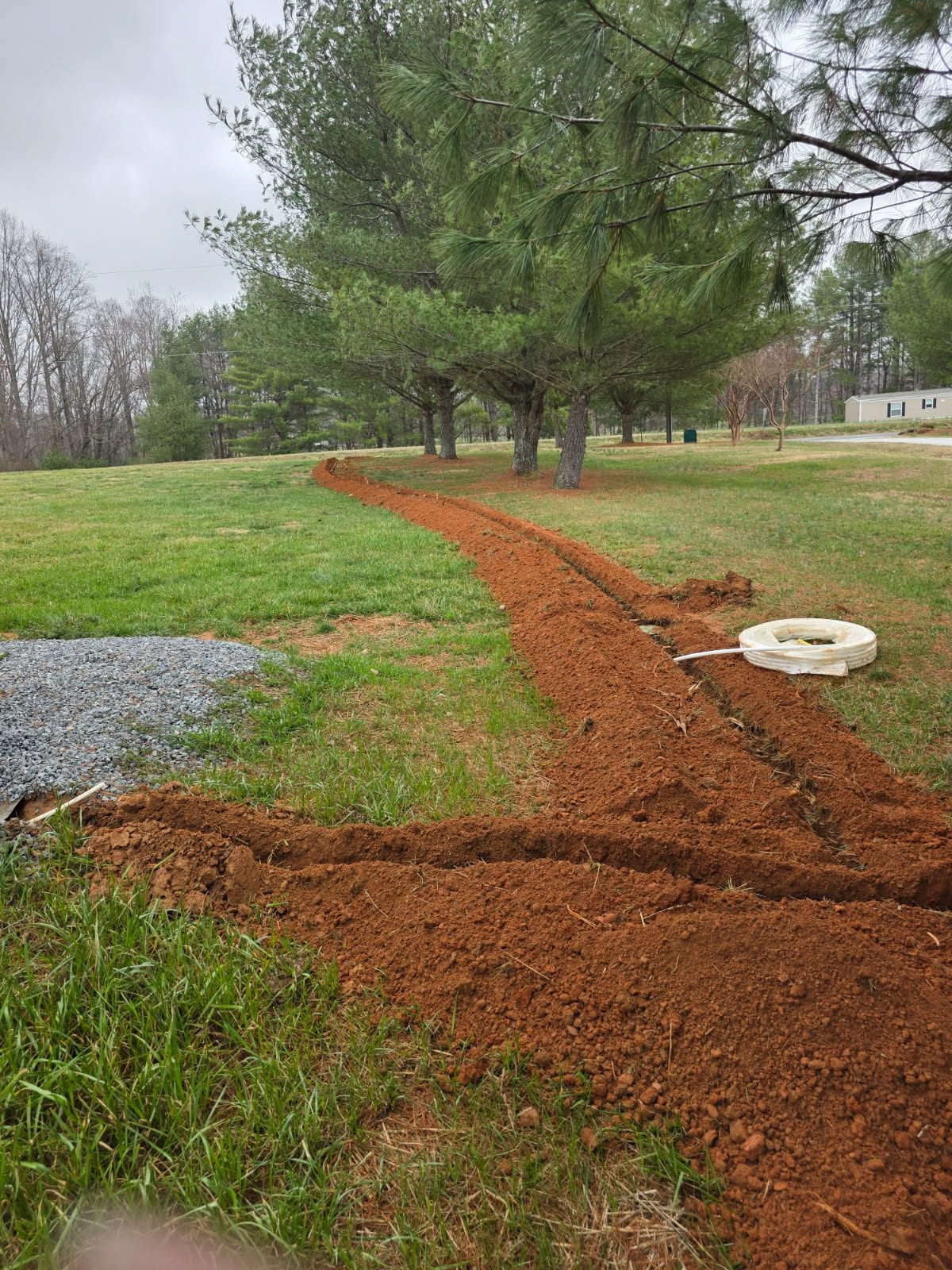 Two intersecting open trenches with a pipe coupling fitting laid beside one trench in an open field.