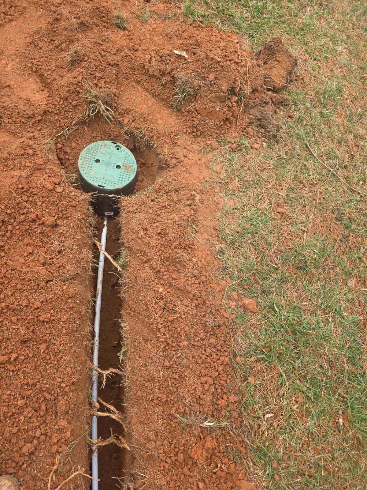 Close-up of a round irrigation valve box set into a soil trench with a supply line running into it.
